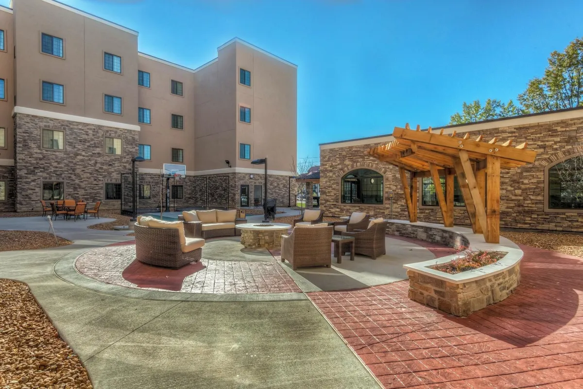 A cozy and beautifully landscaped outdoor patio with a pergola, a fire pit, comfortable seating, and lush greenery. The setting invites guests to relax and gather after a day of exploring the city.