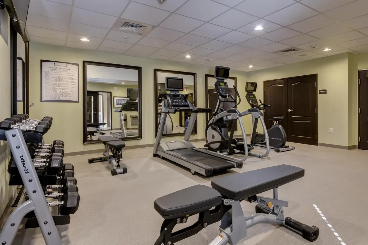 A fitness center equipped with dumbbells, a treadmill, elliptical machine, and large mirrors. The space is clean, well-lit, and inviting, ideal for guests seeking to maintain their fitness routine during their stay.