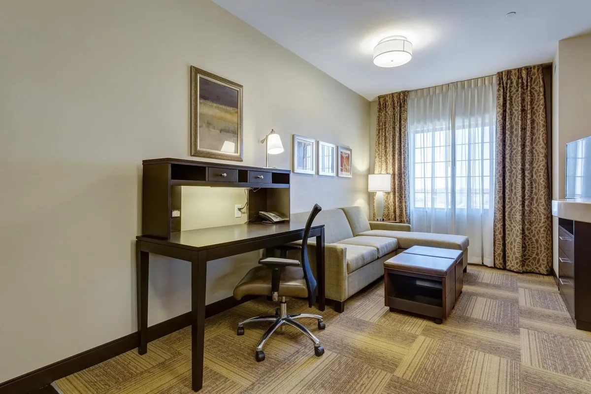 The image showcases a bright, inviting condo interior featuring a comfy sofa, a dedicated work desk with a chair, soft lighting from a table lamp, tasteful artwork on the wall, and a large window with curtains. The scene conveys a sense of both relaxation and productivity, highlighting the perfect blend of comfort and functionality.