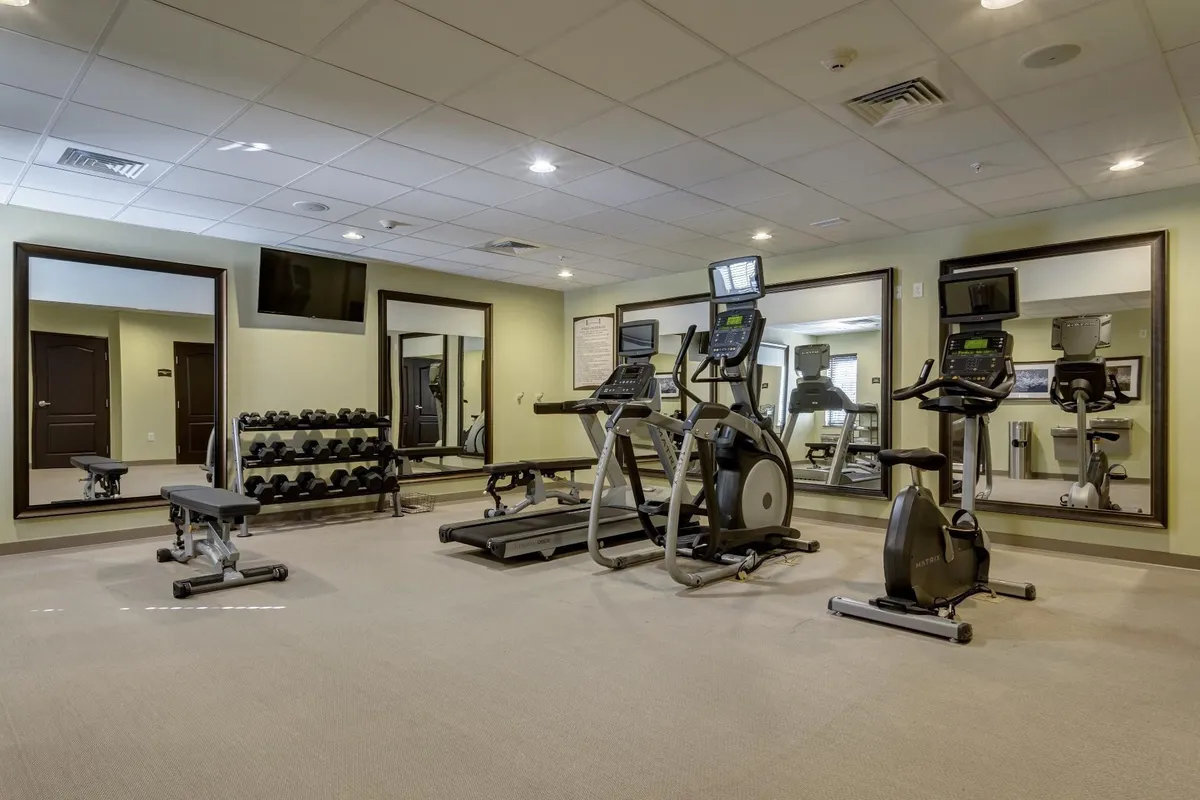 A modern fitness center featuring a row of cardio machines, a fully stocked dumbbell rack, and wall mirrors, creating a dynamic space for guests to exercise or join fitness classes.