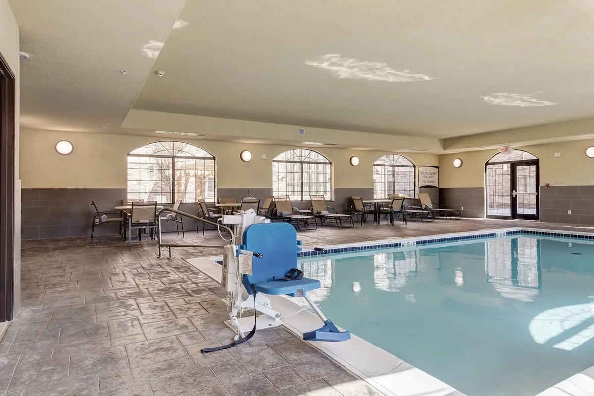This interior image features an inviting indoor swimming pool surrounded by comfortable seating and large windows that let in natural light. A pool lift is visible, showcasing accessibility. The tranquil atmosphere and accessibility features suggest a place of relaxation and respite.