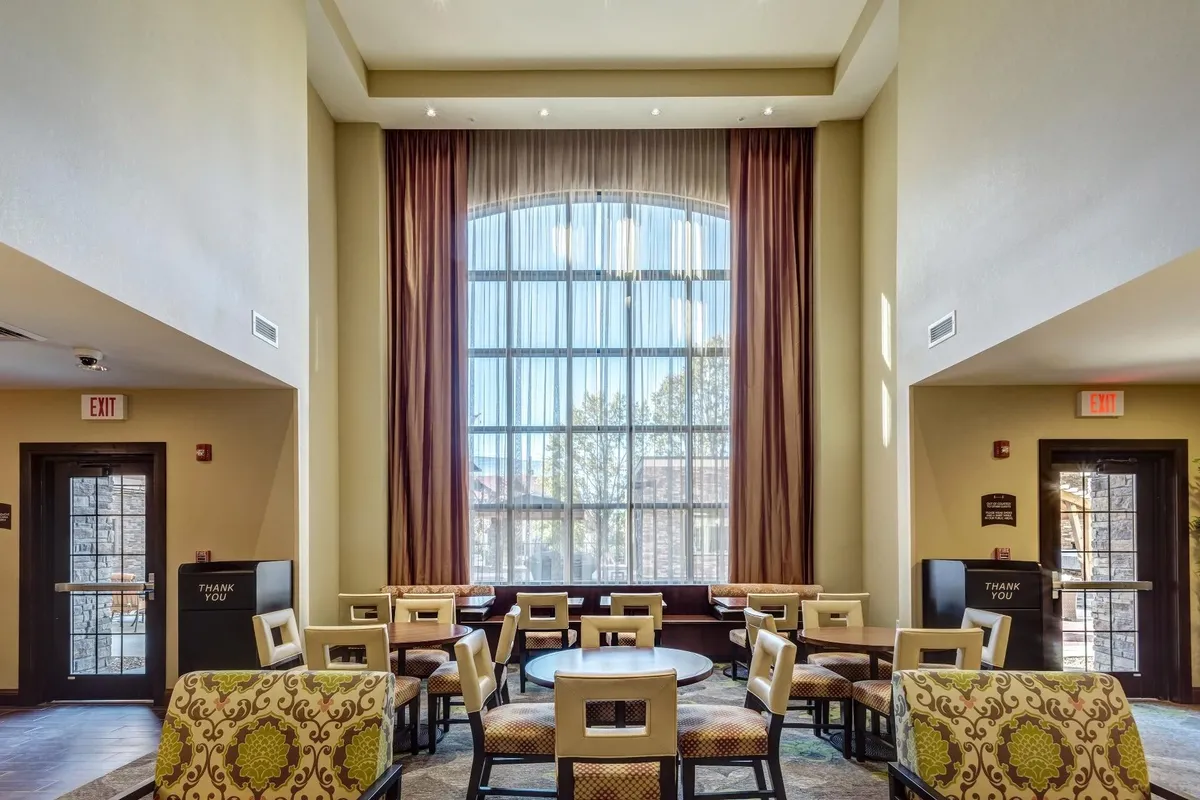 An inviting seating area with a large arched window, comfortable chairs, and decorative curtains. The bright, airy atmosphere is perfect for relaxation, reading, or informal meetings, adding a touch of character to the suite.