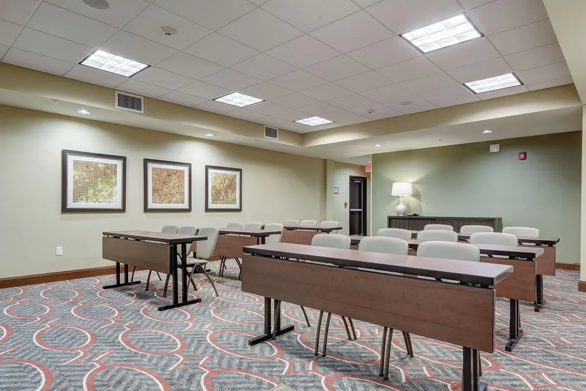 A well-lit meeting room featuring tables arranged for team discussions or workshops, with tasteful artwork on the walls and a modern lamp providing additional ambiance. The setup is conducive to focused work, collaboration, and professional gatherings.