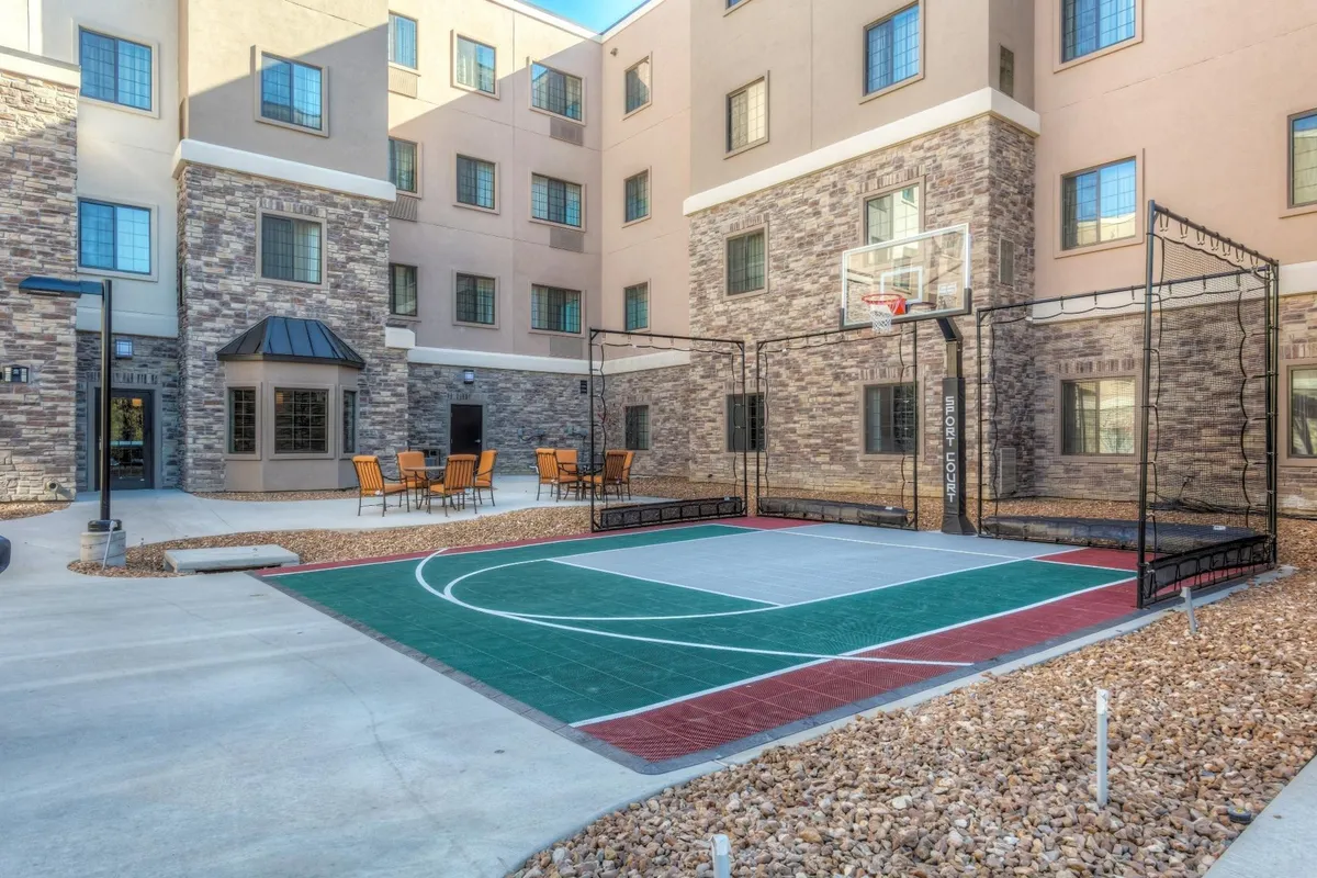 An exterior shot showcasing the hotel's basketball court, outdoor seating area, and building facade. The space is energetic and encourages outdoor play, relaxation, and family bonding.