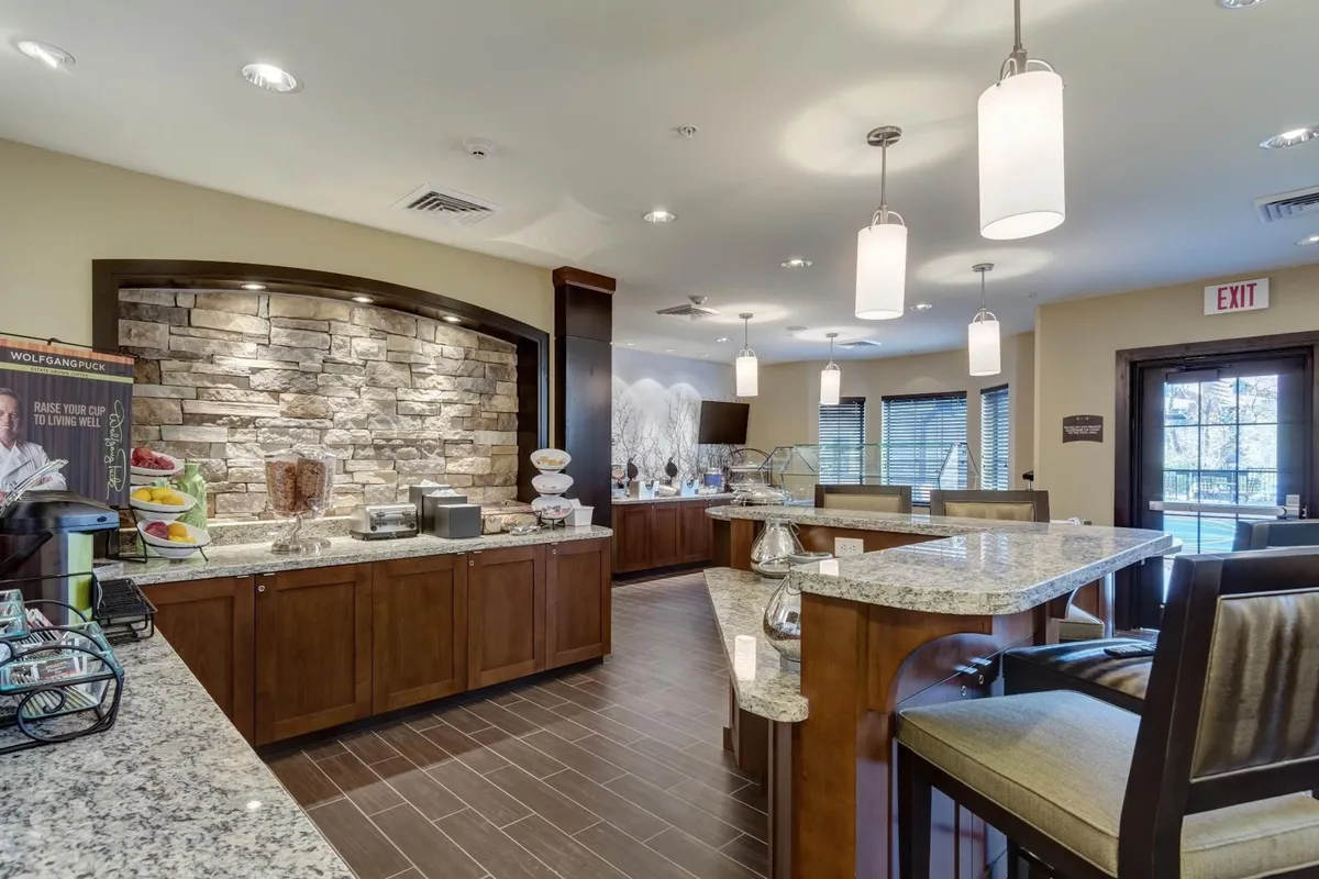 A welcoming breakfast buffet area featuring granite countertops, a stone wall backdrop, and a display of breakfast items. The scene suggests a space where guests can enjoy morning coffee, socialize, and start their day in a communal setting.