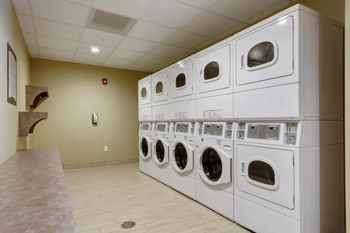 A tidy laundry facility with modern laundry machines, a countertop for folding clothes, and well-organized shelving, offering a glimpse into practical hotel amenities.
